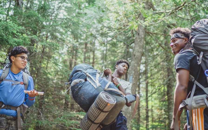 a group of backpacking students stand in a clearing surrounded by green trees on an outward bound expedition 
